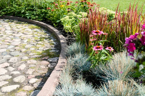 Modern design urban garden landscaping. Flower garden with beautiful flowers near pedestrian stone pathway in the city in sunny day.