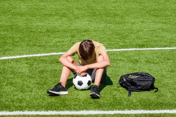 Sad alone teenage boy sitting in empty school sport stadium outdoors. Emotions, defeat, lost game, difficulties, problems of teenagers.