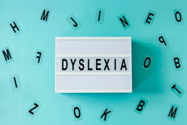 White lightbox with DYSLEXIA word and different letters haphazardly scattered on light blue background. Top view.