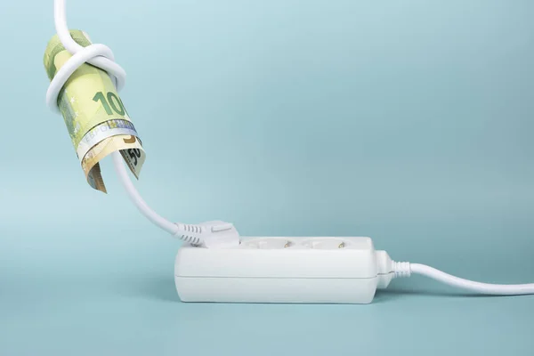 Euro banknote bills tied in knot in electrical power cable and plugged into power strip extension cord on blue background. Increasing electricity cost, rise electric price, expensive energy concept.