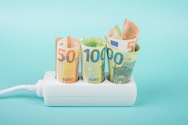 Euro money banknotes plugged in power strip extension cord on light blue background. Electricity prices increasing every month. Rising electric price and expensive energy concept.