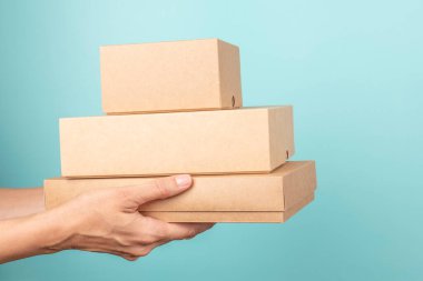 Kadın ellerinde bir yığın karton kutu. Açık mavi arka planda boş kahverengi paket kutuları. Paketleme, alışveriş, ücretsiz nakliye, teslimat konsepti.