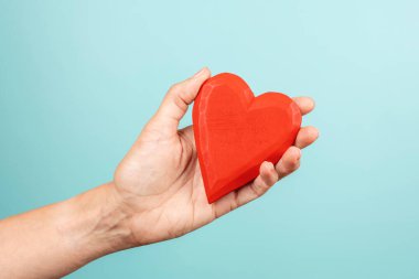 Woman hand holding red wooden heart on light blue background. Love, care, donation concept.
