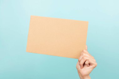 Woman hand holding blank sheet of brown cardboard on light blue background.