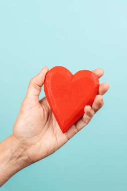 Woman hand holding red wooden heart on light blue background. Love, care, donation concept.