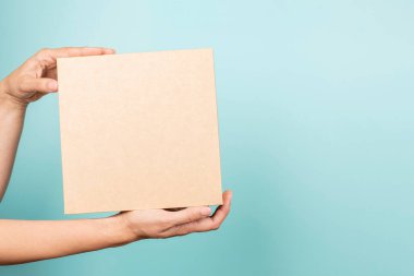 Kadın eli açık mavi arka planda kahverengi dikdörtgen karton kutu gösteriyor. Mokup paket kutusu. Paketleme, alışveriş, teslimat, hediye, hediye konsepti.
