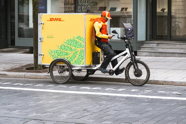 Vilnius, Litvanya, 12 Eylül 2022: Kurye şehre sarı DHL elektrik dağıtım bisikleti ile paket teslim ediyor. Sıfır emisyon için son mil teslimat bisikletleri.