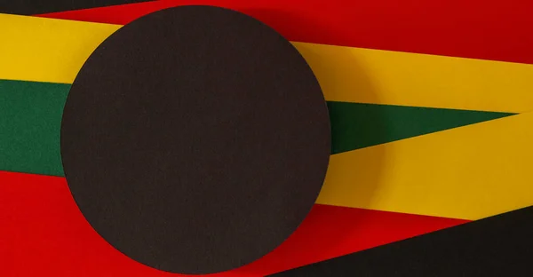 Black History Month color background. Black circle on geometric red, yellow, green color background. Top view.