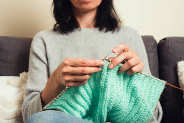 Bambu örgü iğneleri tutan ve yeşil yün kazak ören kadınların ellerini kapatın. Hobi, rahatlama, akıl sağlığı, sürdürülebilir yaşam tarzı.