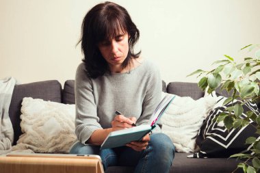 Çevrimiçi çalışma, evde uzaktan öğrenme. Orta yaşlı bir kadının video görüşmesi, online toplantısı, çalışması, öğrenmesi, video eğitimi alması, dijital tablet bilgisayarında çevrimiçi Webinar 'ı olması ve not alması.