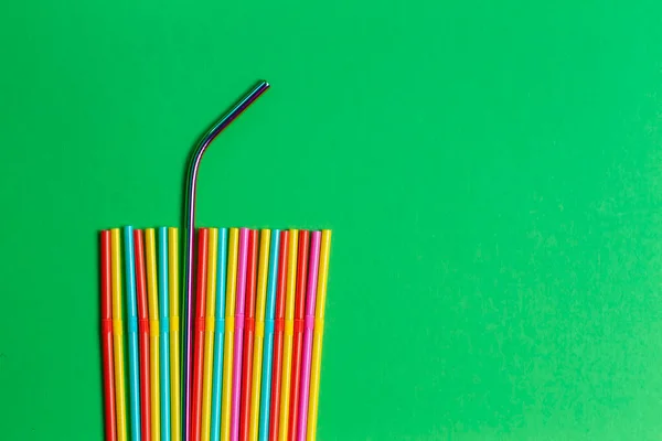 Stainless steel reusable drinking straw with plastic straws on green background.