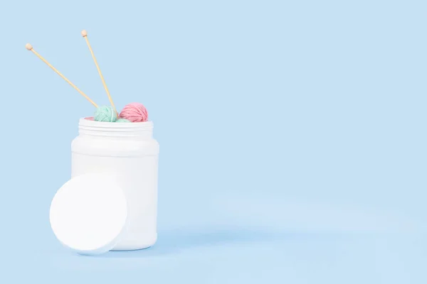 Knitting as therapy. Supplement bottle with thread yarn balls and knitting needles on a light blue background. Knitting health benefits, stress reduction, wellbeing, mental health.