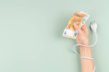 Elektrik kablosu, elinde Euroo banknotları tutan kadının eline dolandı. Enerji verimliliği, enerji tüketimi, artan elektrik fiyatı ve pahalı enerji kavramı.