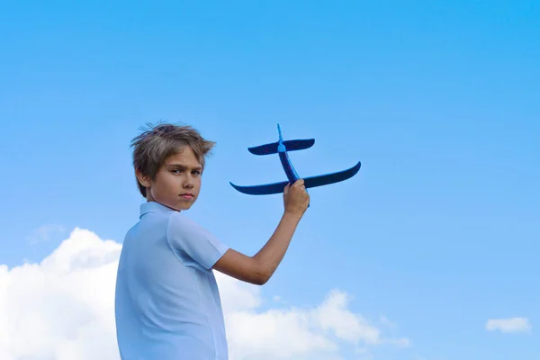 Child throwing toy plane. Kid holding plane and looking direct to the camera. Boy playing with blue toy airplane against blue sky on sunny day outdoors.