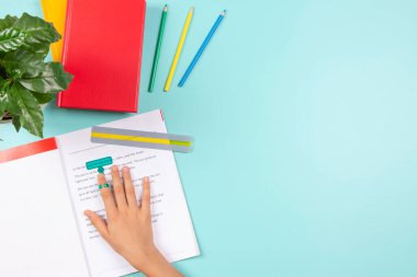Child affected by dyslexia doing homework, reading book using colored rulers overlays strips. Blue desk with books and school supplies. Education, learning disability, reading difficulties concept