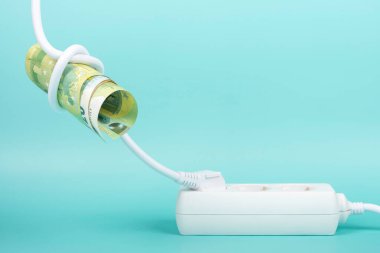 Euro banknote bills tied in knot in electrical power cable and plugged into power strip extension cord on blue background. Increasing electricity cost, rise electric price, expensive energy concept.