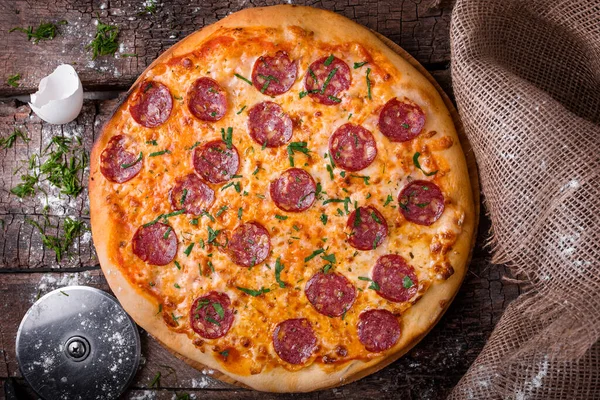 Pizza sajtos kolbászos szalámival és fűszernövényekkel fapadlón — Stock Fotó