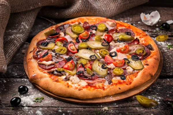 Pizza szalámis barbecue kolbásszal sonka paradicsom harangpaprika egy fapadlón liszttel megszórva — Stock Fotó