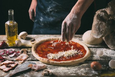 Şef pizza tabanına mozzarella peyniri serpiyor. Geleneksel bir Akdeniz yemeği hazırlarken, yakın plan koyu ahşap bir arka plan elde.