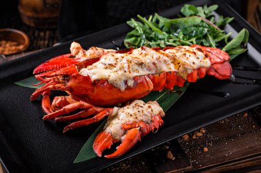 Büyük ızgara ıstakoz eti, siyah tabakta roka yapraklı.