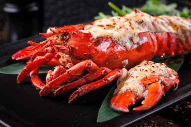 Büyük ızgara ıstakoz eti, siyah tabakta roka yapraklı.