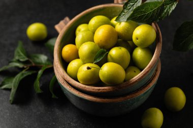 Sarı, yeni koparılmış kiraz eriği, yeşil yapraklı, seramik bardaklarda gri arka planda, yakın planda.