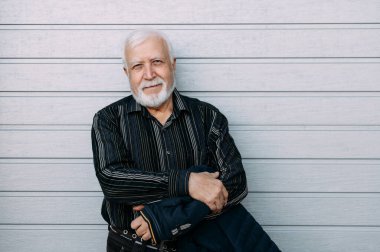 Yaşlı gri saçlı adam kameraya katlanmış elleriyle bakıyor, orta plan, gri çizgili arka plan, mesaj için boş alan