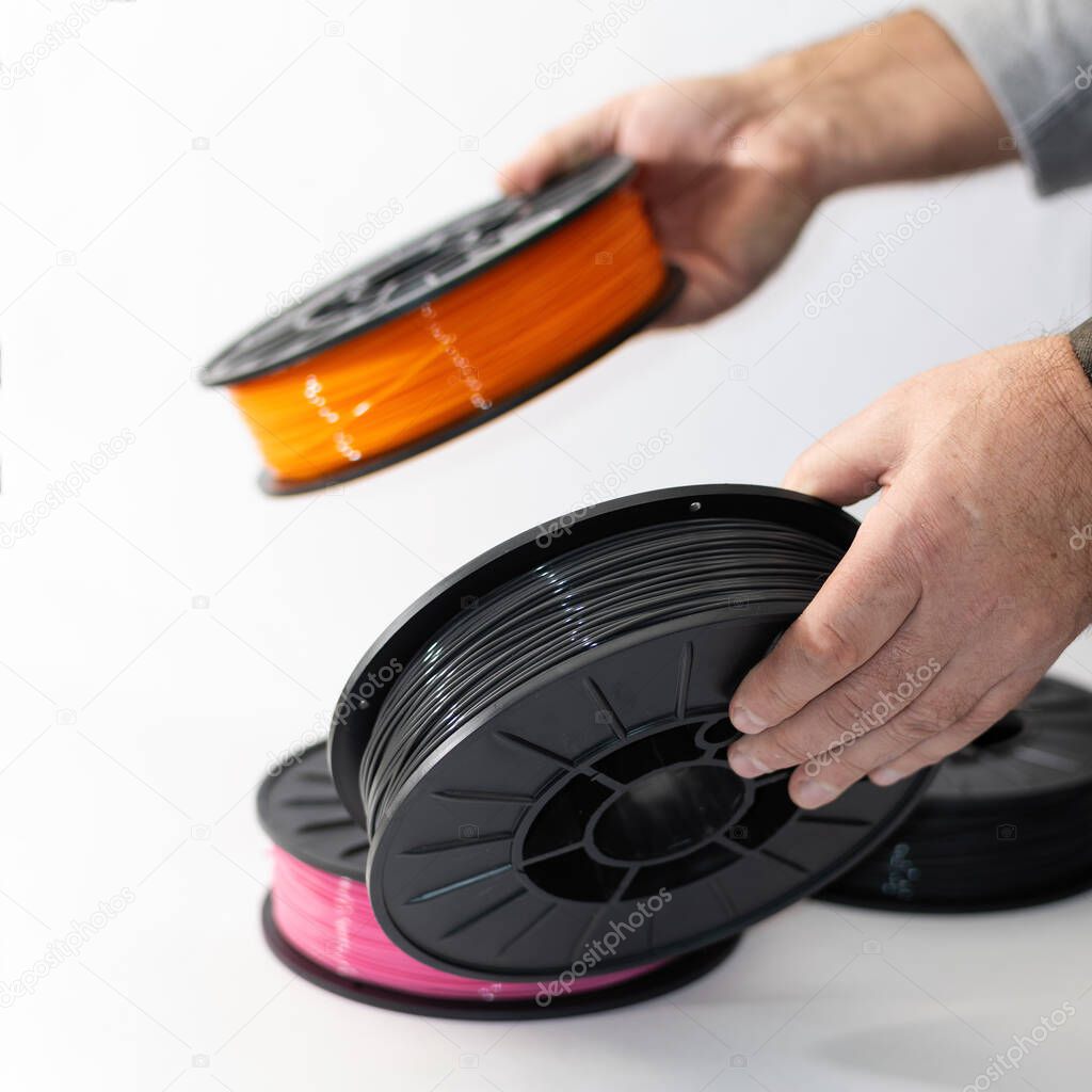 hands hold colored spools with plastic for 3D printing