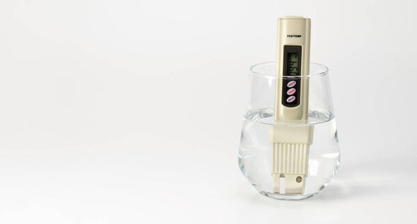 ТДС измеритель физраствора в стакане воды на белом фоне. Счетчик соли. Анализатор качества питьевой воды. Место для текста