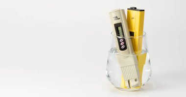 Su kalite kontrolü için bir metre pH ölçer ve TDS. Beyaz arka planda bir bardak suda tuz sayacı ve pH ölçer. Su sertliği, tuz ölçer. Su kalitesi analizcisi içiyorum. Metin için yer