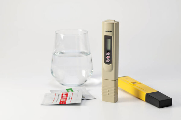 Набор счетчиков pH и TDS для контроля качества воды. Солемер и pH метр в стакане воды на белом фоне. Твердость воды, солемер. Анализатор качества питьевой воды. Место для текста