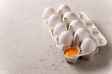 Hafif arka planda tavuklu beyaz yumurtalar, bir yumurta kırılır ve sarısı görülür, yazı için boş alan, arka taraf ışığı