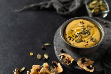 lentil and champignon cream soup with croutons and pumpkin seeds on a dark gray background