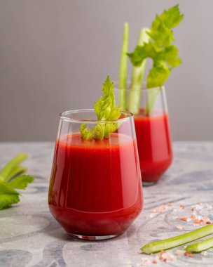 tomato juice in a glass glass with chopped celery on a light gray background, close-up