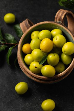 Sarı, yeni koparılmış kiraz eriği, yeşil yapraklı, seramik bardaklarda gri arka planda, yakın planda.