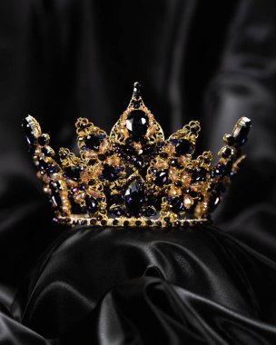 Güzellik kraliçesi için taç, güç ve zarafetin sembolü, rekabet, gösteri. Siyah örtülü saten arka planda sarı metal ve mavi taşlı diadem
