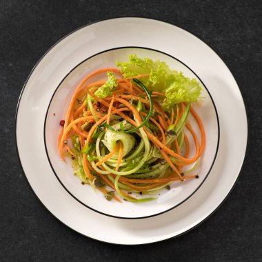 Beyaz tabakta salatalıklı taze sebze salatası ve gri arka plan, üst manzara, yakın çekim.