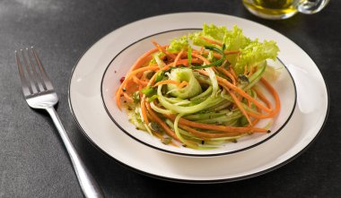 Beyaz bir tabakta salatalıklı taze sebze salatası ve gri arka plan, servis ediliyor, yakın çekim.