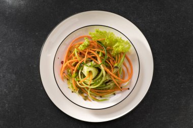 Beyaz tabakta salatalıklı taze sebze salatası ve gri arka plan, üst manzara, yakın çekim.