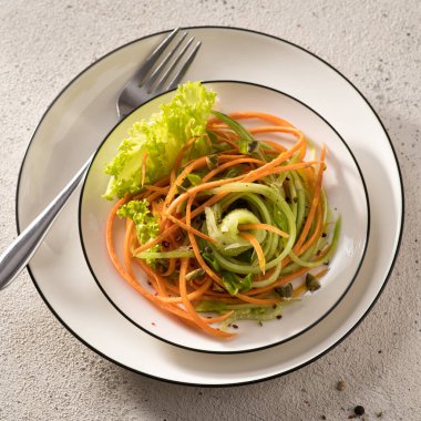 Beyaz bir tabakta salatalıklı taze sebze salatası, çatal, açık arkaplan, yakın plan, kare format, üst manzara.