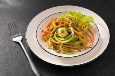 Beyaz bir tabakta salatalıklı taze sebze salatası ve gri arka plan, servis ediliyor, yakın çekim.