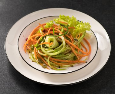 Beyaz bir tabakta salatalıklı taze sebze salatası ve gri arka plan, servis ediliyor, yakın çekim.