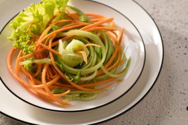 Taze sebze renginde havuç salatası, salatalık ve otlar beyaz bir tabakta, makro, hafif arka plan, yakın plan, üst görüş