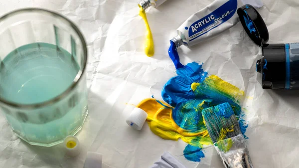 Boya ve fırça, sarı-mavi ve yeşil renkli parlak bir nokta, bir bardak su.