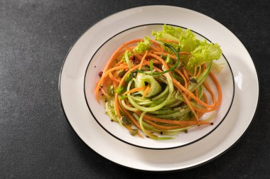 Beyaz bir tabakta salatalıklı taze sebze salatası ve gri arka plan, servis ediliyor, yakın çekim.