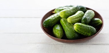 Beyaz ahşap arka planda bir kasede salatalıklar, pankart, metin için yer