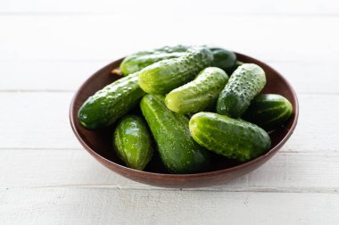 fresh cucumbers in a bowl on a white wooden background