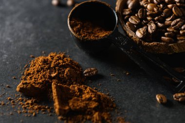 coffee beans in a coconut bowl with ground coffee are scattered on the table on a dark gray background, close-up