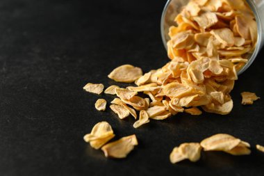 Koyu gri arka planda cam bir kasede dilimlenmiş sarımsak, mesaj için boş alan.