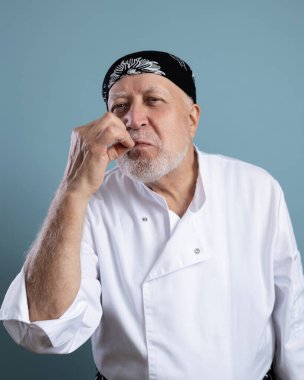 Kıdemli karizmatik erkek şef açık mavi arka planda kameraya bakıyor.